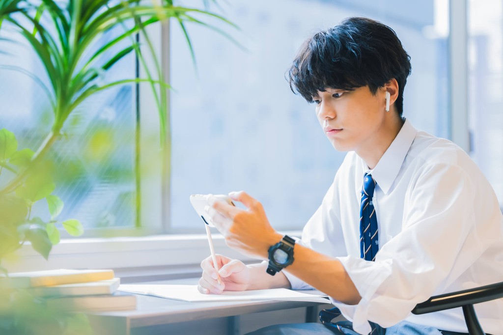 イヤホンを着け、スマホを見ながらメモを取る学生