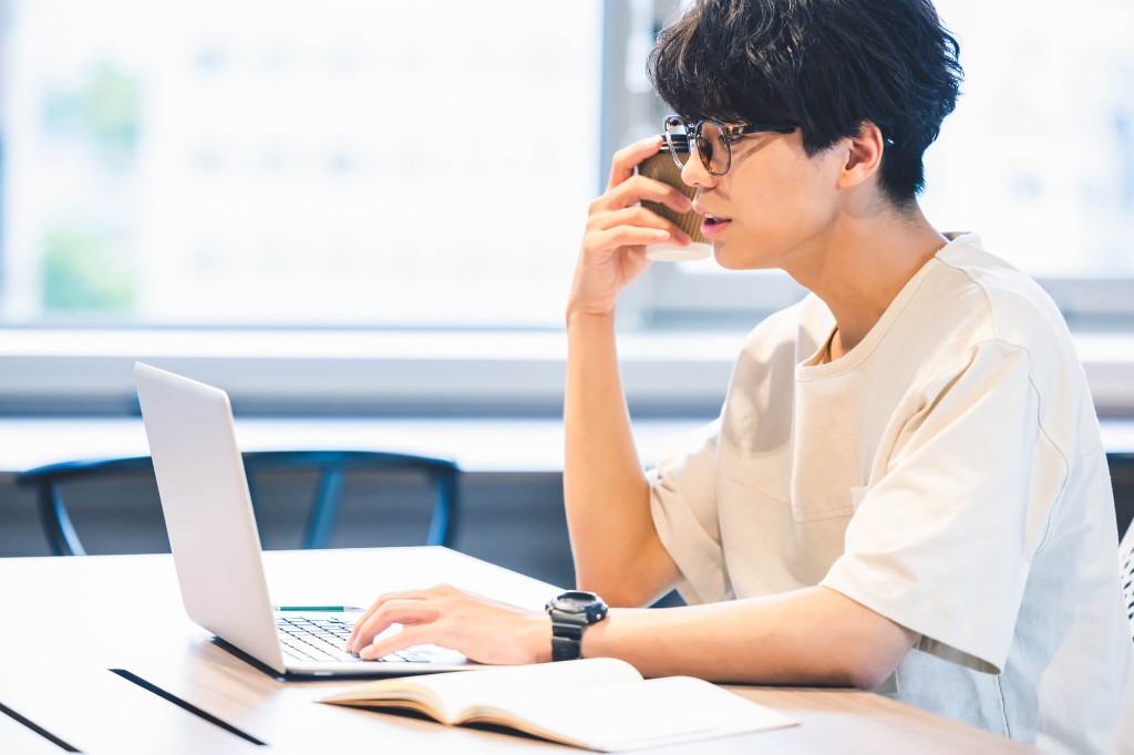 眼鏡をかけて、コーヒーを飲みながらパソコンで学習する男性
