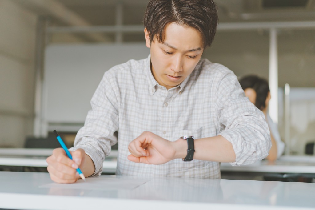 鉛筆を持ち、腕時計を確認しながら学習する男性