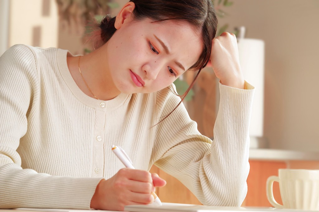 ペンを手に、机で考えながら書く女性