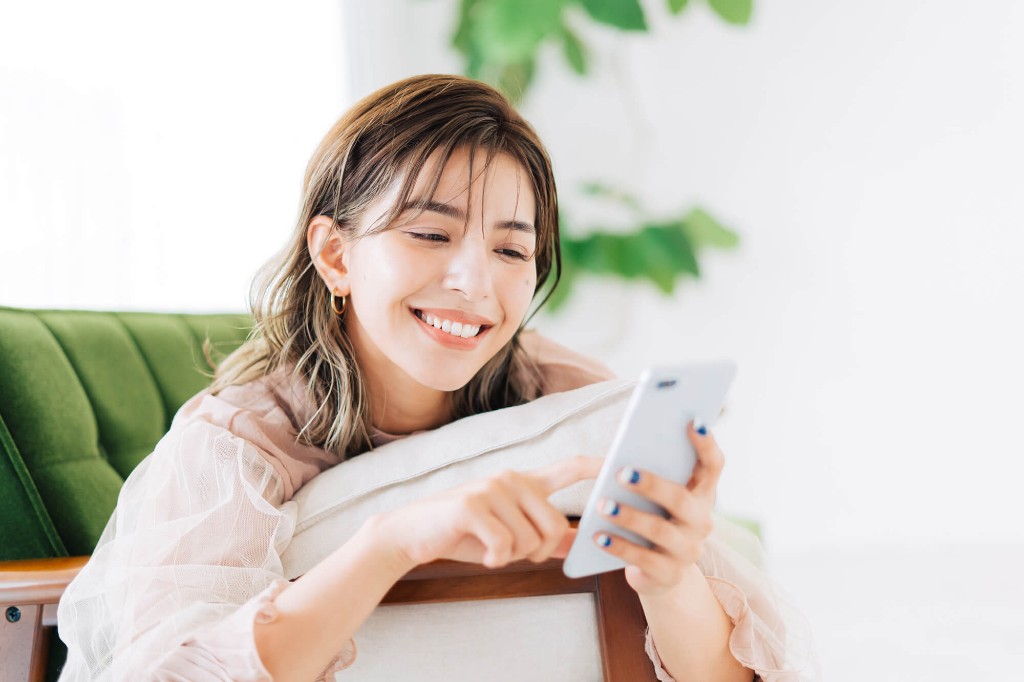 ソファでスマホを見て笑う女性