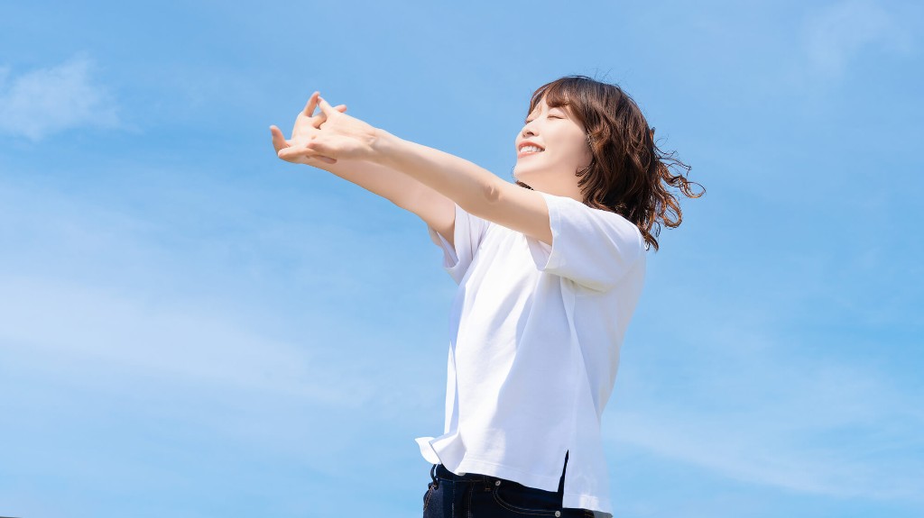 青空の下で両手を広げて笑う女性