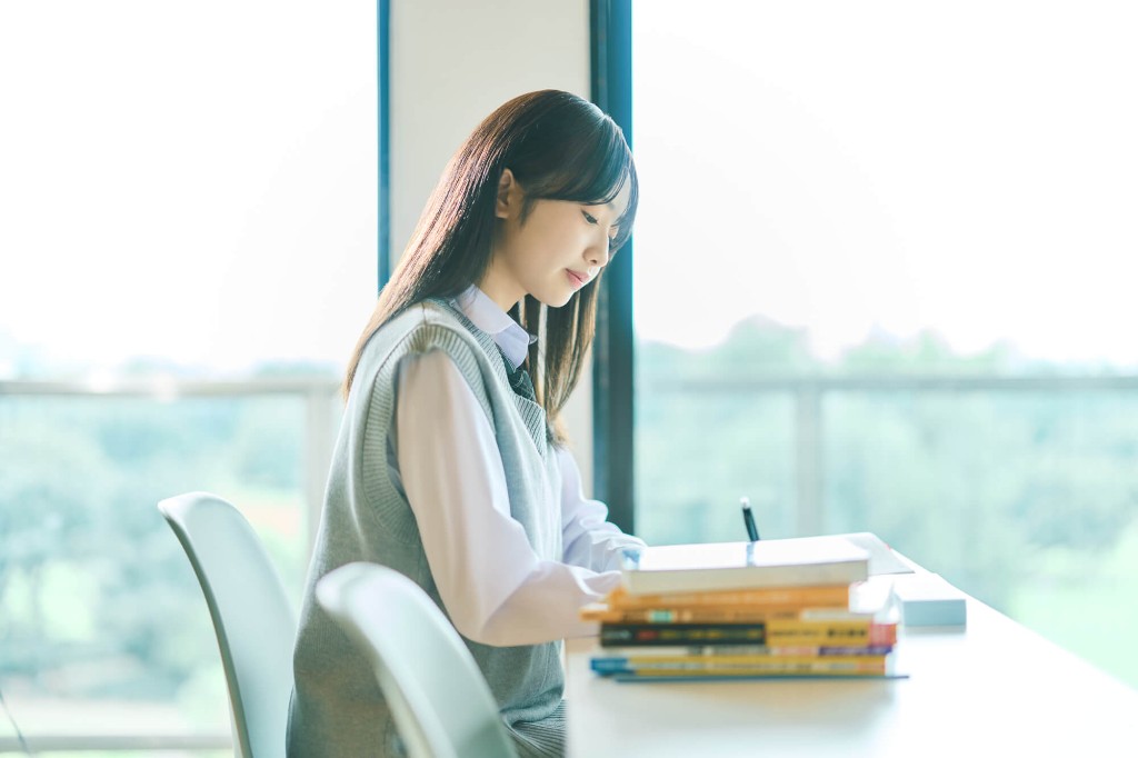 窓際で参考書を開いて学習する高校生
