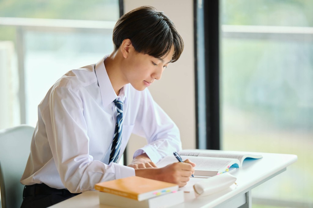 机でノートに書きながら学習する高校生