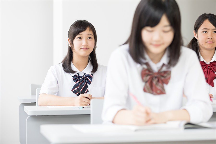 教室でノートを取りながら学ぶ制服の中学生
