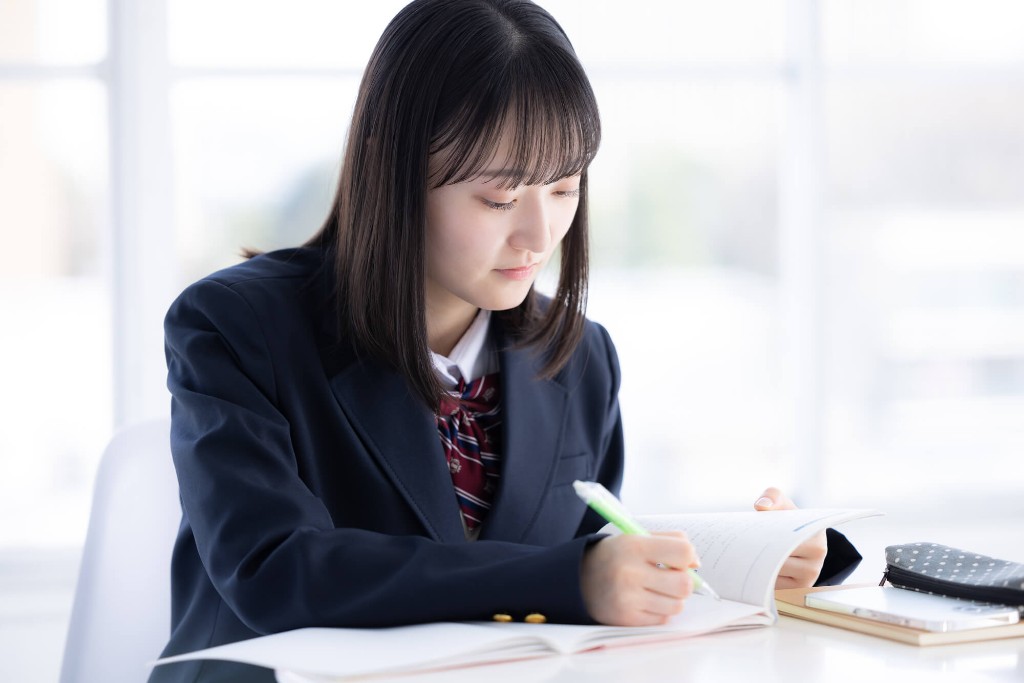 制服でノートに書きながら学習する高校生