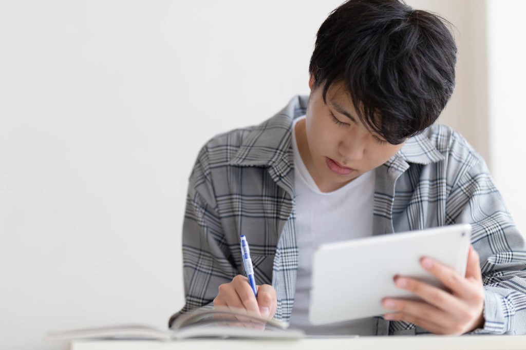 タブレットを見ながらノートに書く高校生